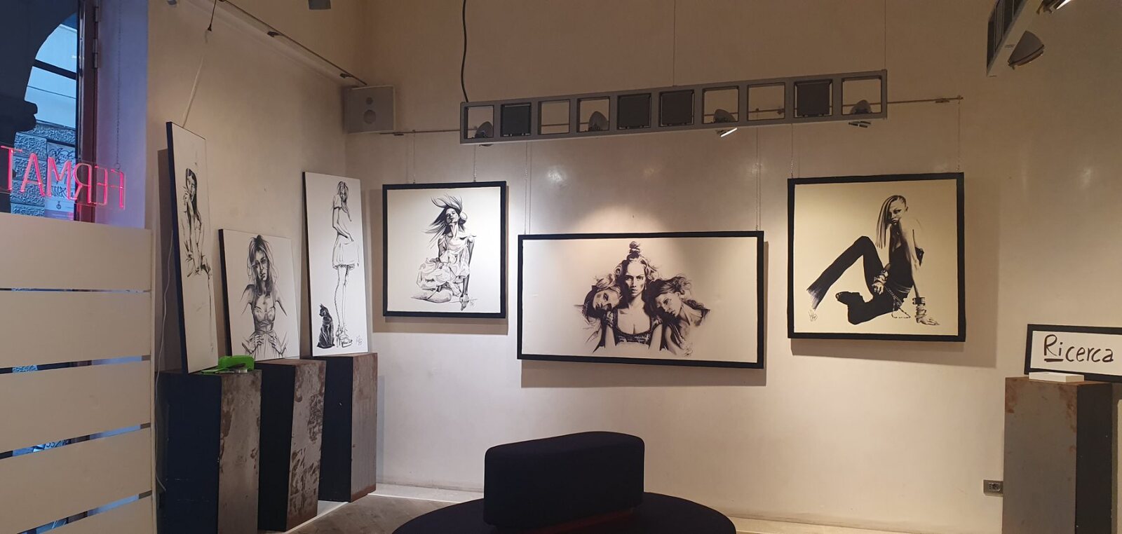 La parete con i disegni incorniciati in bianco e nero e il cartello «Ricerca».