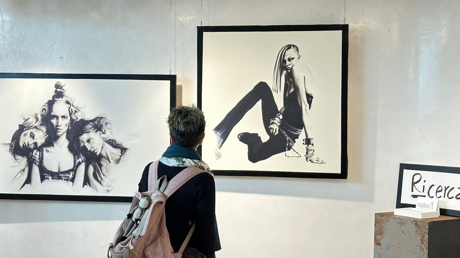 Una visitatrice osserva da vicino un disegno in bianco e nero incorniciato.
