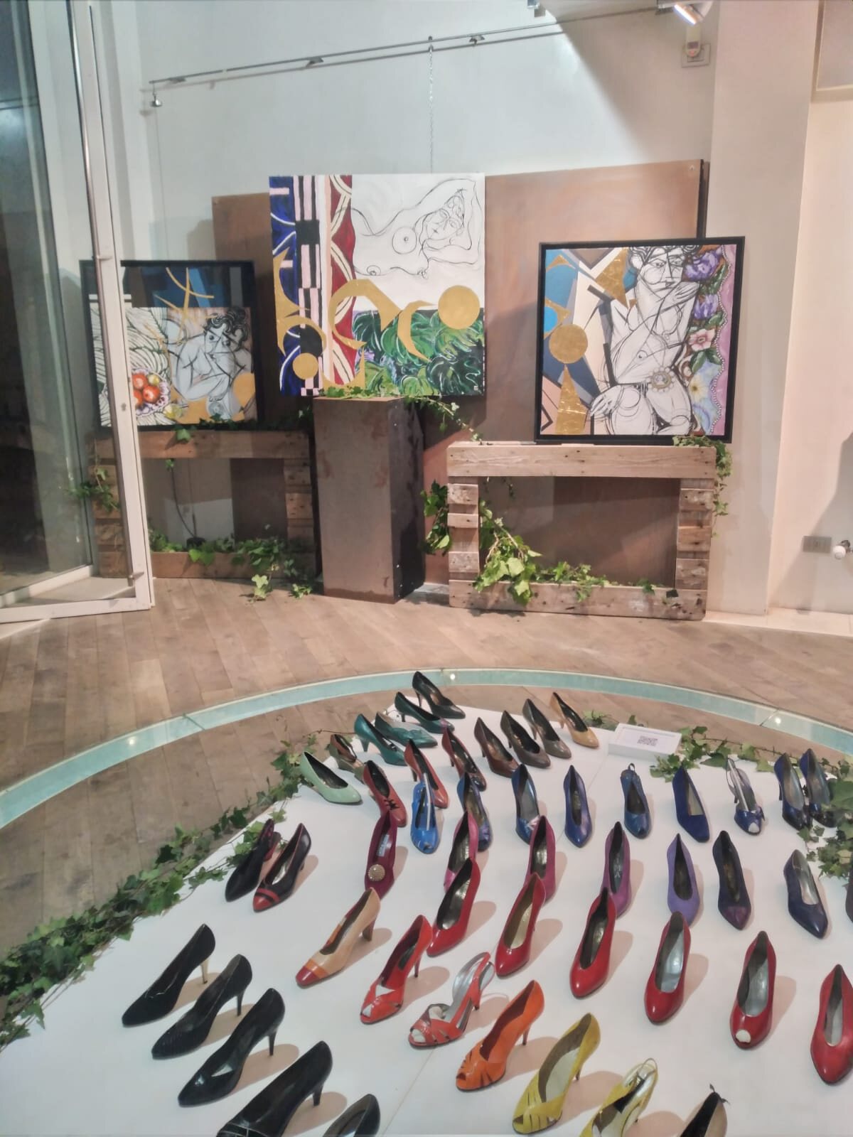Dettaglio dell’installazione: le scarpe colorate disposte in semicerchio davanti alle opere.