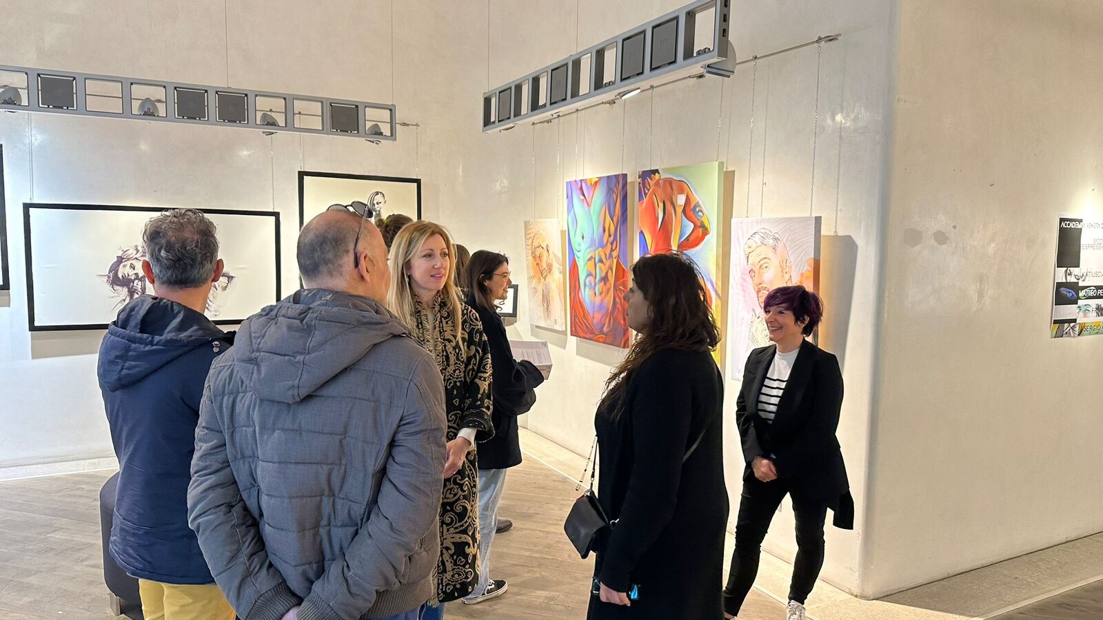 Visitatori in conversazione davanti ai quadri esposti.