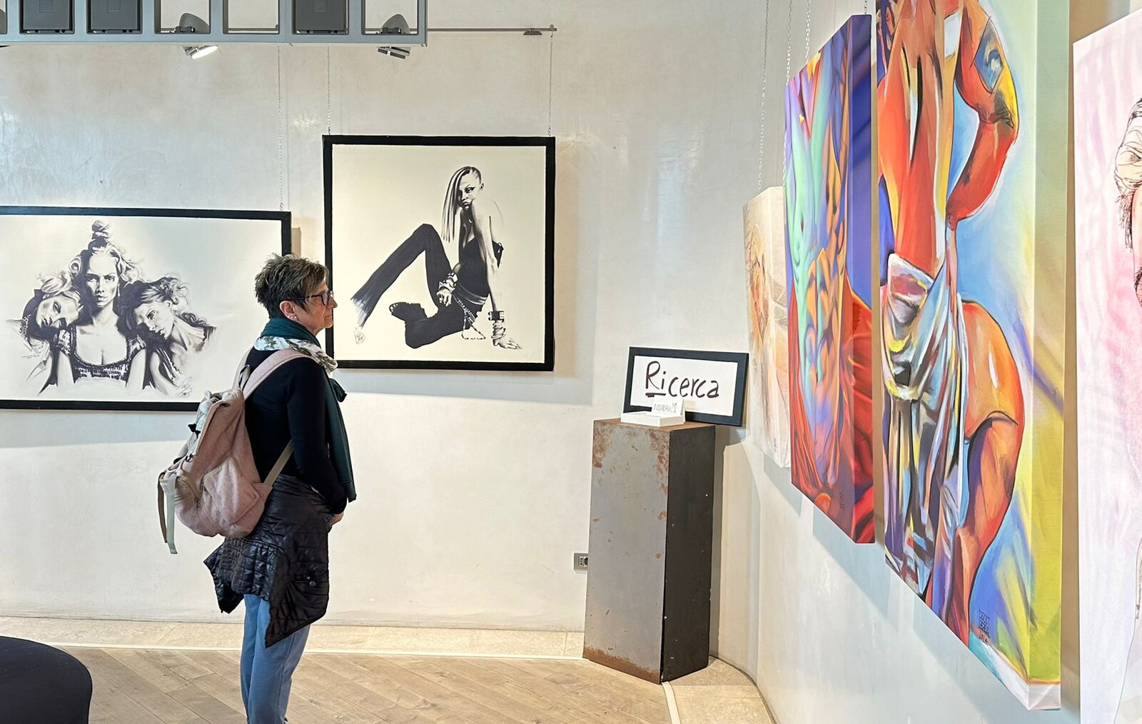 Una visitatrice davanti ai disegni in bianco e nero e a una grande tela colorata, accanto al cartello «Ricerca».