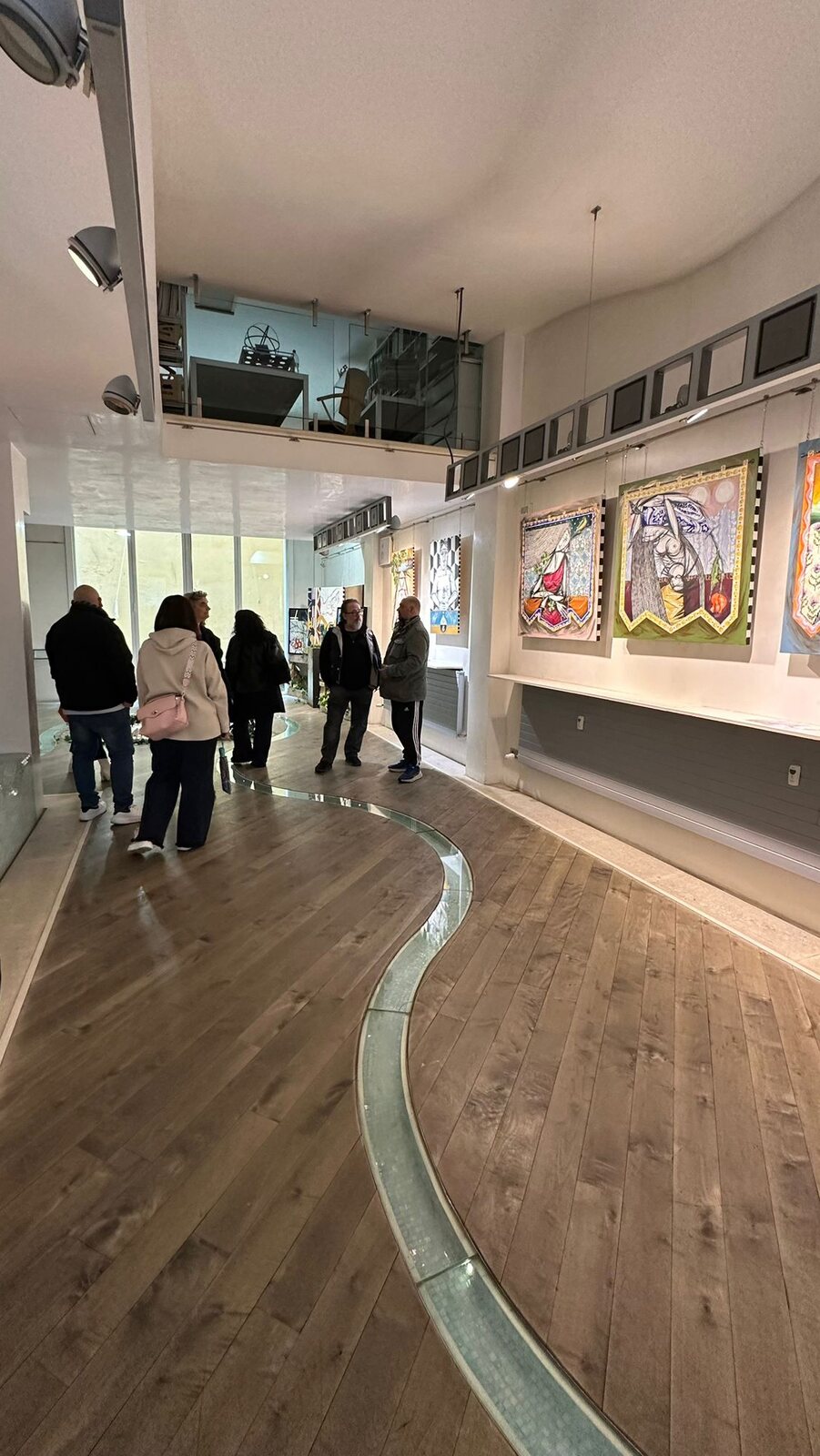 Visitatori nella sala, lungo la linea curva che attraversa il pavimento dell’allestimento.